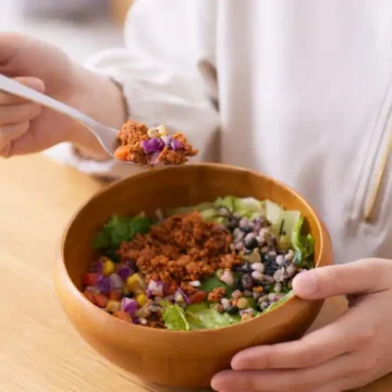 Person eating a colorful anti-inflammatory salad bowl with beans, greens, and chopped vegetables