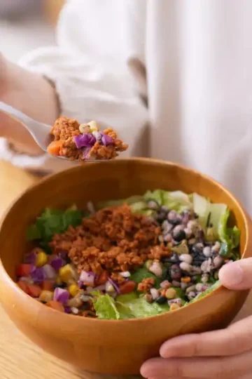 Person eating a colorful anti-inflammatory salad bowl with beans, greens, and chopped vegetables