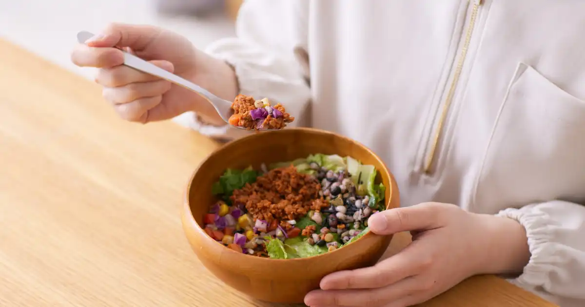Person eating a colorful anti-inflammatory salad bowl with beans, greens, and chopped vegetables