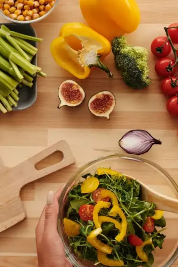 Top-down view of a beginner preparing a colorful plant-based anti-inflammatory salad with fresh vegetables and whole ingredients on a wooden surface.