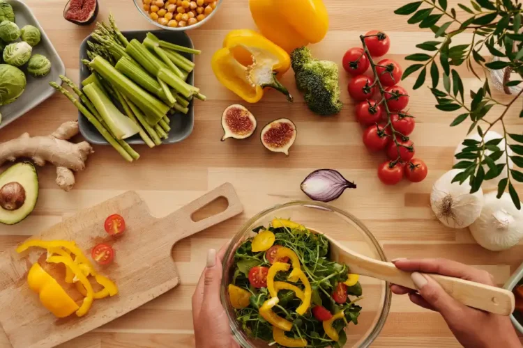 Top-down view of a beginner preparing a colorful plant-based anti-inflammatory salad with fresh vegetables and whole ingredients on a wooden surface.