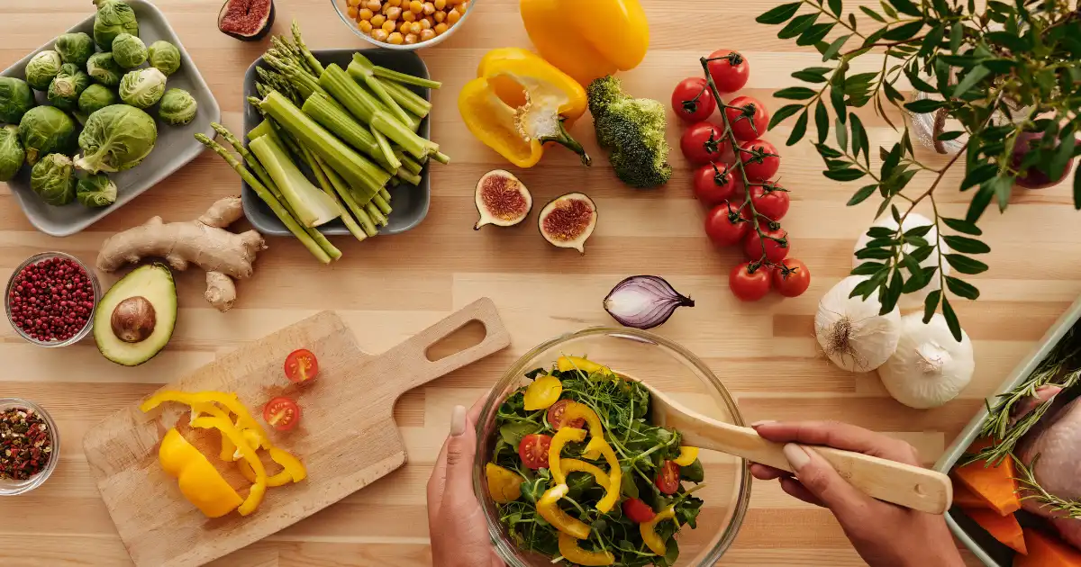 Top-down view of a beginner preparing a colorful plant-based anti-inflammatory salad with fresh vegetables and whole ingredients on a wooden surface.