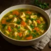Steaming bowl of anti inflammatory chicken soup with turmeric broth, tender chicken, carrots, celery, and fresh parsley on a rustic wooden table.