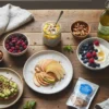 Rustic wooden table with anti-inflammatory snacks including avocado toast, apple slices with almond butter, chia pudding, yogurt with berries, walnuts, green tea, and a tuna pouch.