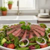 Chimichurri steak salad with grilled flank steak slices over fresh greens, cherry tomatoes, avocado, and red onion topped with vibrant green chimichurri sauce in a white bowl.